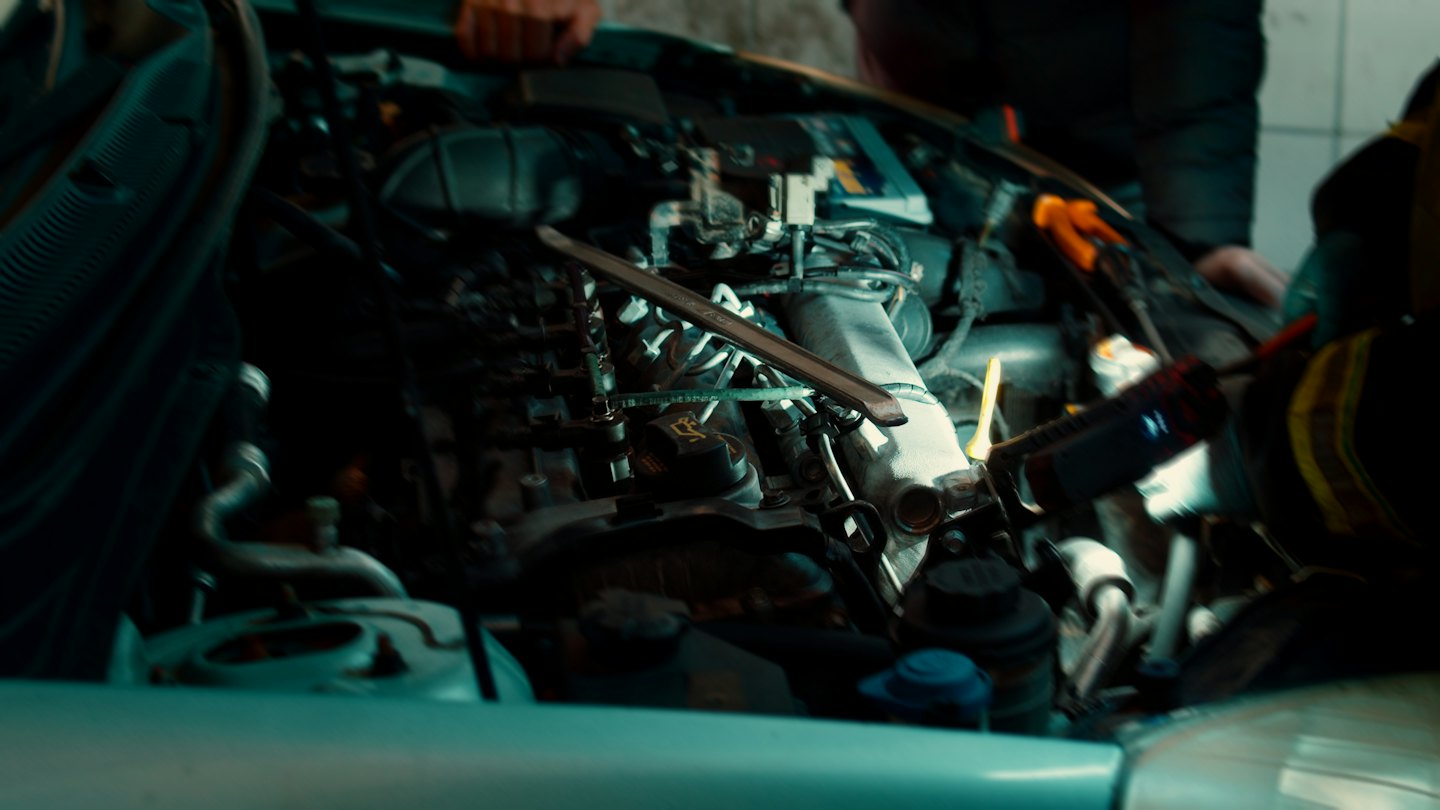 Hände arbeiten an einem Automotor mit einer Taschenlampe.